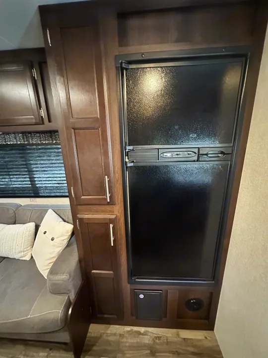 Inside an rv rental: View of the kitchen/living area with a large black refrigerator, dark wood cabinetry, and a comfortable sofa.. Jayco Jay Flight SLX 2020