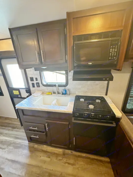 This RV rental kitchen features a sink, microwave, stove, and dark cabinetry, ideal for travel adventures.. Jayco Jay Flight SLX 2020