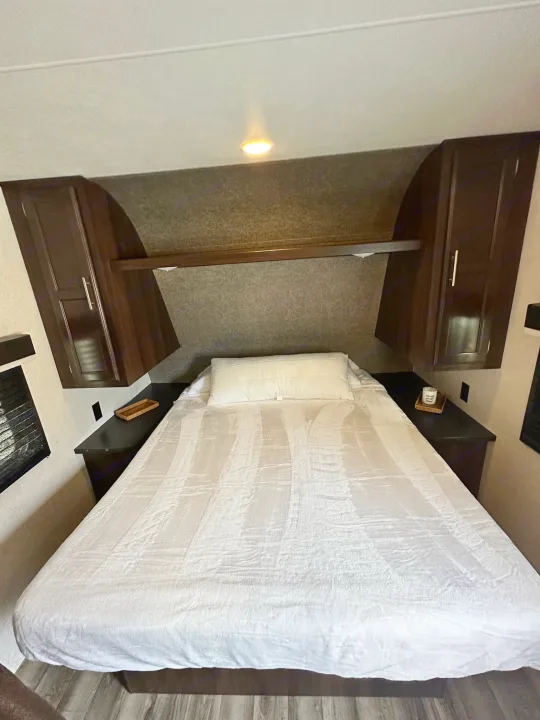 This RV rental's cozy bedroom features a white queen bed, dark wood overhead cabinets, and convenient side storage.. Jayco Jay Flight SLX 2020