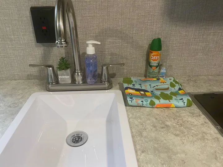 RV rental sink area: includes faucet, soap, a 'Welcome' plant, bug spray, and camping-themed towel. Ready for trips!. Jayco Jay Flight SLX STX Edition 2022