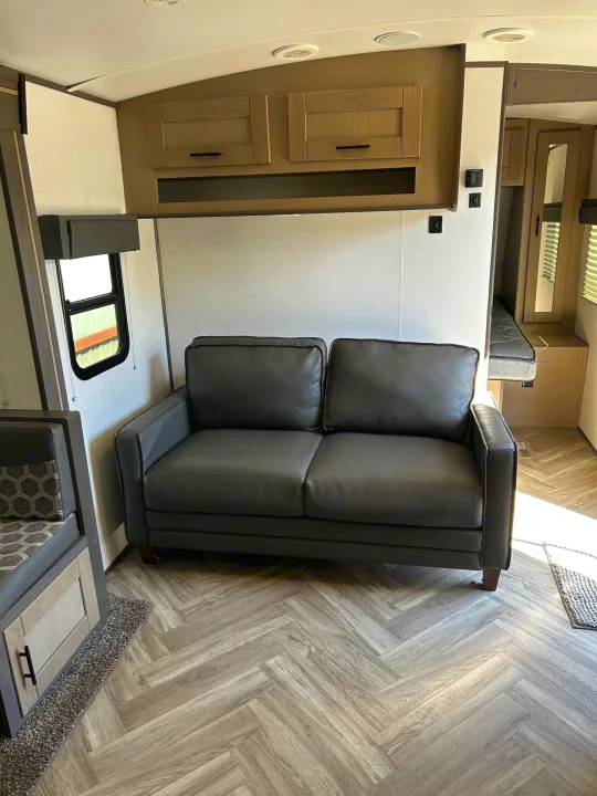 Modern RV rental interior: a comfy sofa, overhead cabinets, and herringbone flooring create an ideal compact living space.. Cruiser Rv Corp Shadow Cruiser 259BHS 2021