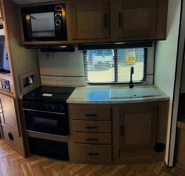 Step inside this clean RV rental kitchen, equipped with a microwave, stove, oven, sink, and light wood cabinets.. Cruiser Rv Corp Shadow Cruiser 259BHS 2021