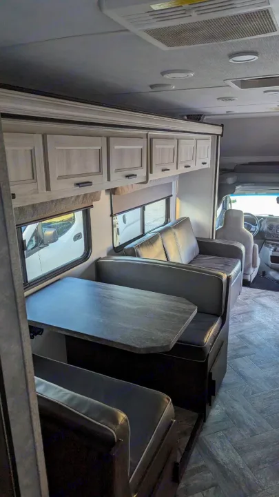 RV rental interior showcases a cozy dinette, sofa, and light wood cabinets, with a driver's area visible forward.. Forest River Sunseeker LE 2022