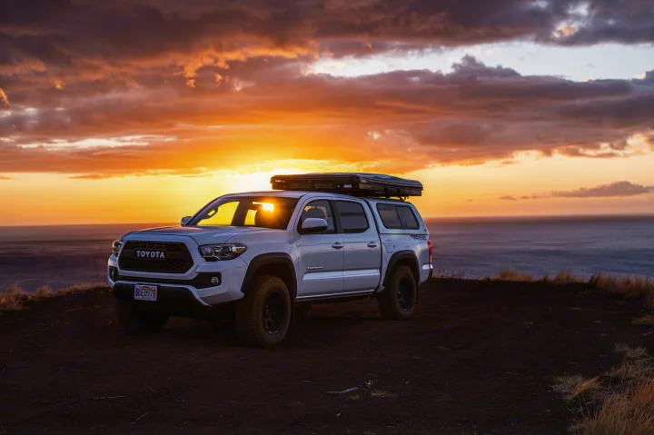 White Toyota Tacoma with rooftop tent overlooking the ocean at sunset. Perfect rv rental for overlanding adventures.. Custom Camper 2016