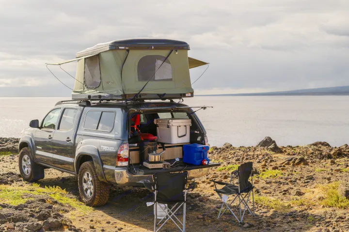 Overland RV rental: A dark pickup truck with a rooftop tent and tailgate camp kitchen by a vast body of water.. Other Other 2013