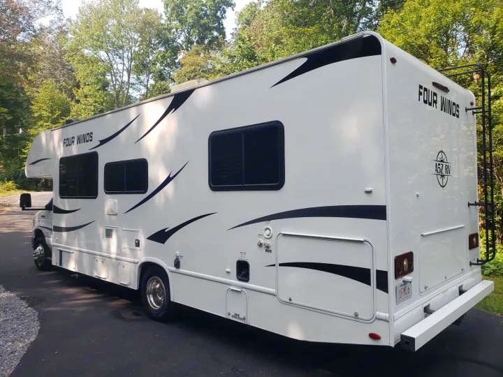 This clean white Four Winds motorhome, ideal for rv rental, is seen parked. It features striking black graphic decals.. Thor Four Winds 2021