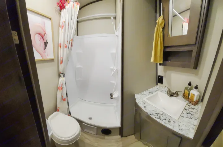 Clean RV rental bathroom featuring a toilet, spacious shower with flamingo curtain, and a modern sink vanity.. Other Other 2019