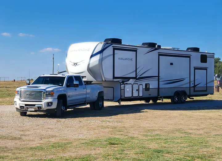 A powerful GMC truck is hitched to a large Avalanche fifth-wheel RV, offering spacious accommodations for an RV rental or travel.. Keystone RV Avalanche 2023