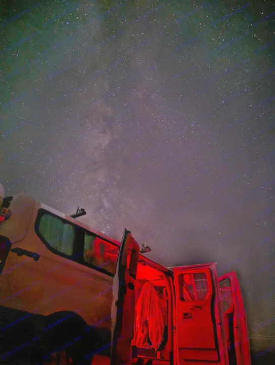 An RV rental's red glow lights up the interior under a starry Milky Way. Perfect for night sky adventures & camping.. Ford Transit 2016