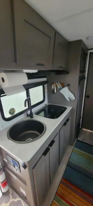 Compact RV rental kitchen interior featuring a modern sink, stovetop, overhead cabinets, and a colorful striped rug.. Heartland RVs Mallard 2022