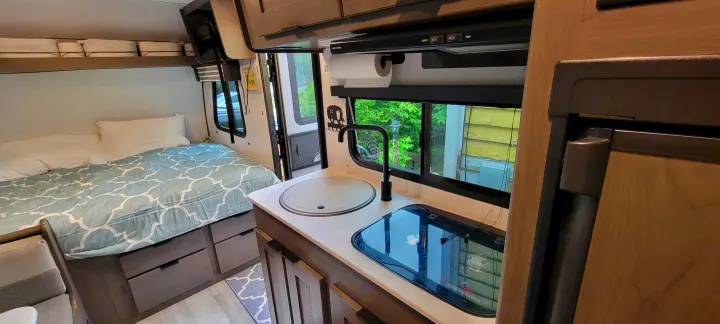 Cozy RV rental interior: bed with storage, compact kitchen with sink, stove, and fridge, offering a functional living space.. Heartland RVs Mallard 2022