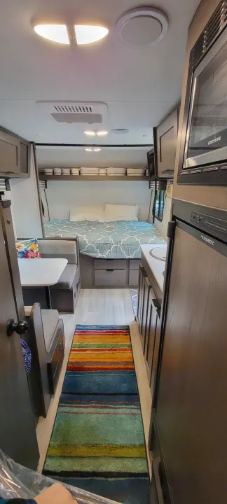 Cozy RV rental interior featuring a compact bedroom, dining area, kitchen with appliances, and a vibrant striped rug.. Heartland RVs Mallard 2022