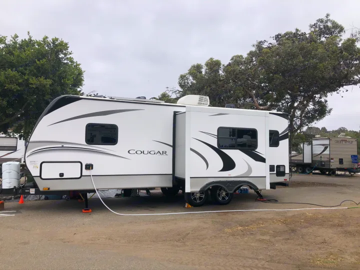 White Cougar RV rental with extended slide-out, parked on gravel with hookups at a camp site. Ready for your travel adventure.. Keystone RV Cougar 2021
