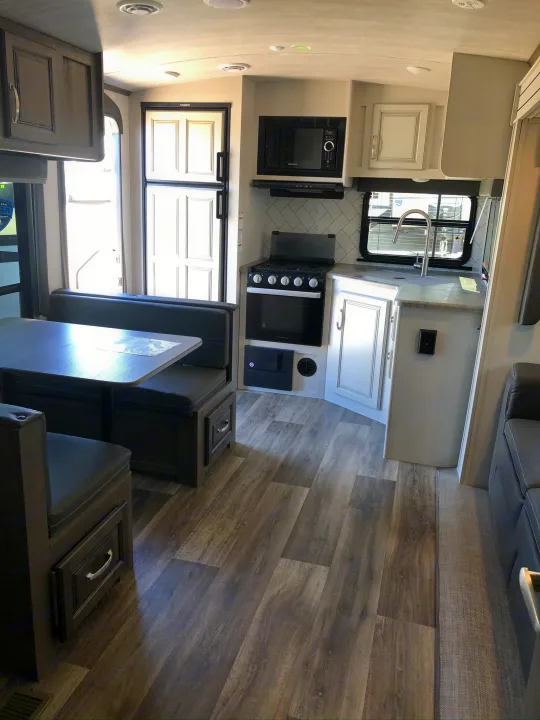 Modern RV rental interior featuring a compact kitchen, dining booth, and wood-look flooring.. Keystone RV Cougar 2021