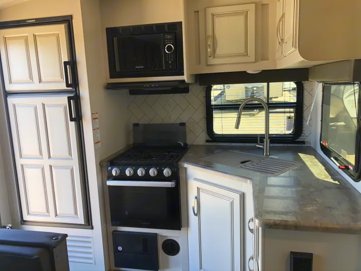 Modern RV rental kitchen: Dometic fridge, Greystone microwave, Furrion oven/stove, sink, gray counters, and white cabinets.. Keystone RV Cougar 2021