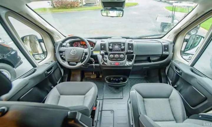 Detailed view of an RV rental's spacious cockpit, showing the Ram dashboard, steering wheel, and comfortable front seats.. Winnebago Solis 2023