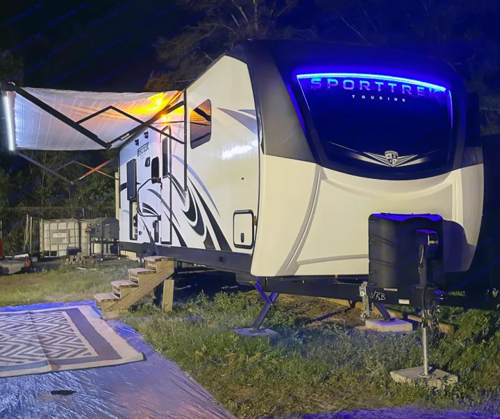 Sporttrek travel trailer RV rental lit up at night with blue front lights and warm awning lights, ideal for camping.. Sport Trek Touring 2021