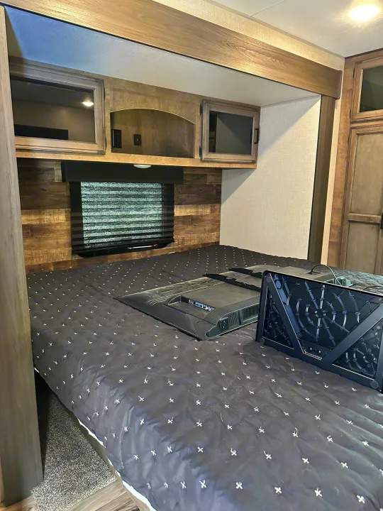 Inside an RV rental: a compact bedroom with a queen bed, window, overhead storage, and a TV on the bed for travelers.. Sport Trek Touring 2021