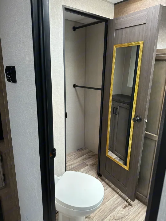 Compact RV rental bathroom and storage area, showing a white toilet, mirrored door, and open wardrobe.. Sport Trek Touring 2021