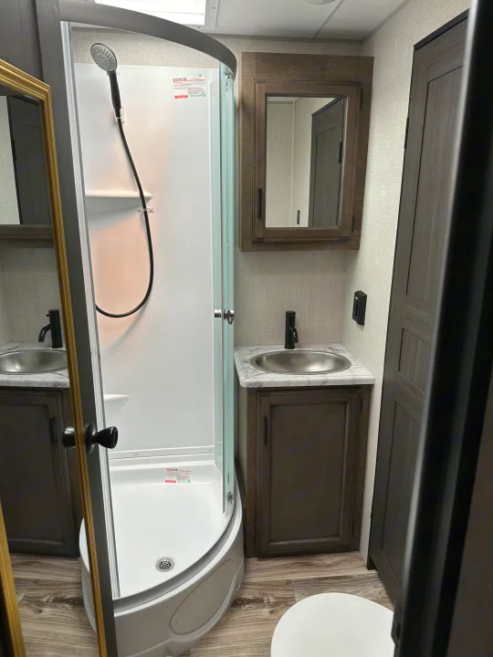 Compact RV rental bathroom with a corner shower, vanity, sink, and dark wood accents. Designed for comfort on the go.. Sport Trek Touring 2021