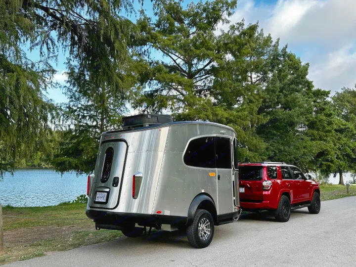 Red SUV towing a sleek silver Airstream camper by the water. Explore nature with this RV rental setup!. Airstream Basecamp 2023