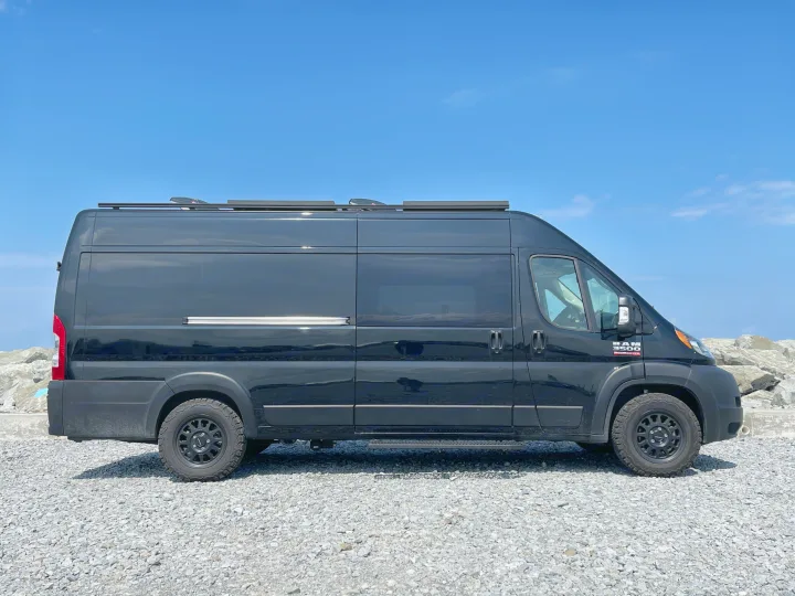 Black Ram ProMaster 3500 RV rental, a customized camper van, on gravel. Clear blue sky.. RAM Promaster 2022