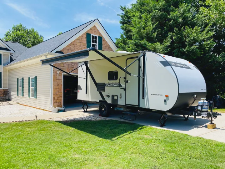 RV rental travel trailer parked in a sunny driveway next to a house with its awning extended.. Forest River Salem FSX 2020
