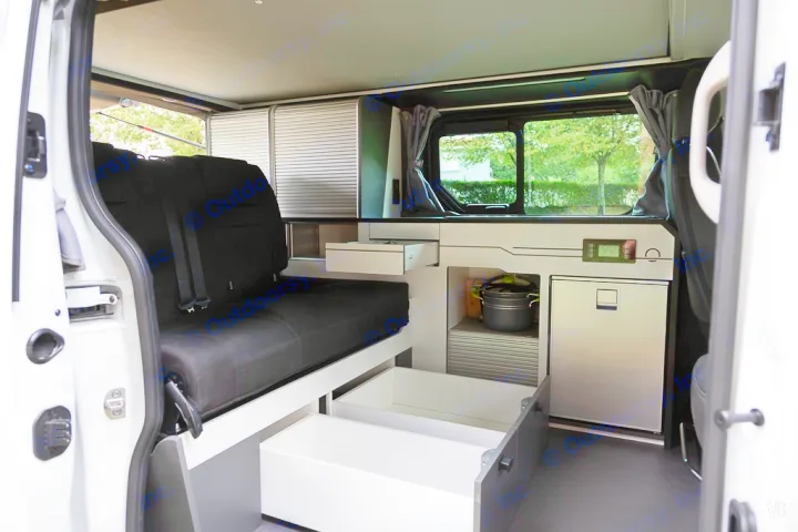 Modern RV rental interior with a black seat, modular storage including open drawers, a small fridge, and a display.. HANROAD TREK 4 2024