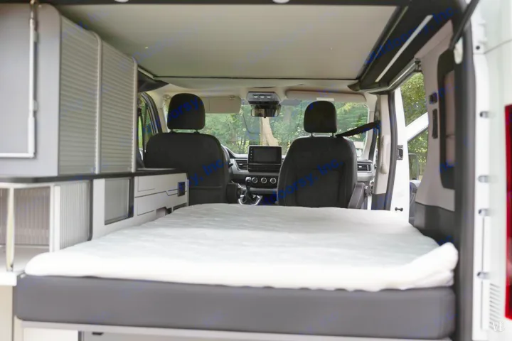 Spacious RV rental interior showing a comfortable bed, ready for travel. Storage cabinets are visible on the left.. HANROAD TREK 4 2024