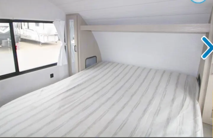 View of an RV rental's bedroom: striped bed, window, and built-in storage.. Forest River Wildwood XLite View 2024