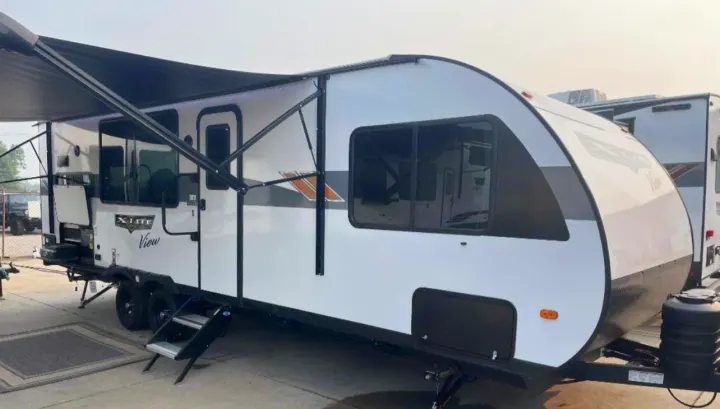 A pristine white and black travel trailer with an extended awning and steps down, ideal for your next rv rental.. Forest River Wildwood XLite View 2024