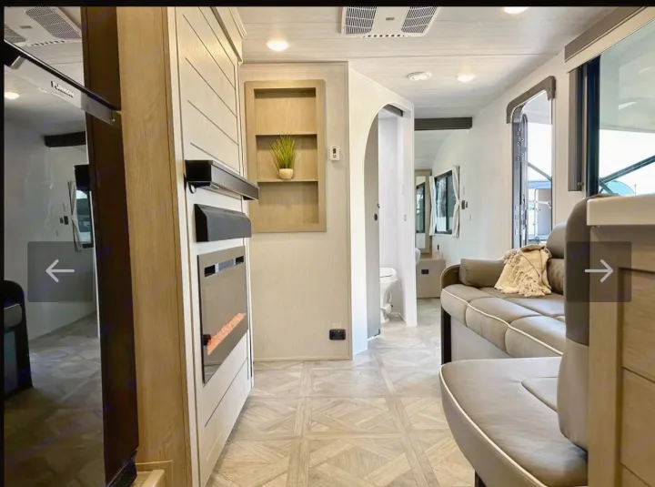 Inside this RV rental: a modern living area with a sofa, fireplace, and kitchen amenities. Beyond, access to a compact bathroom.. Forest River Wildwood XLite View 2024