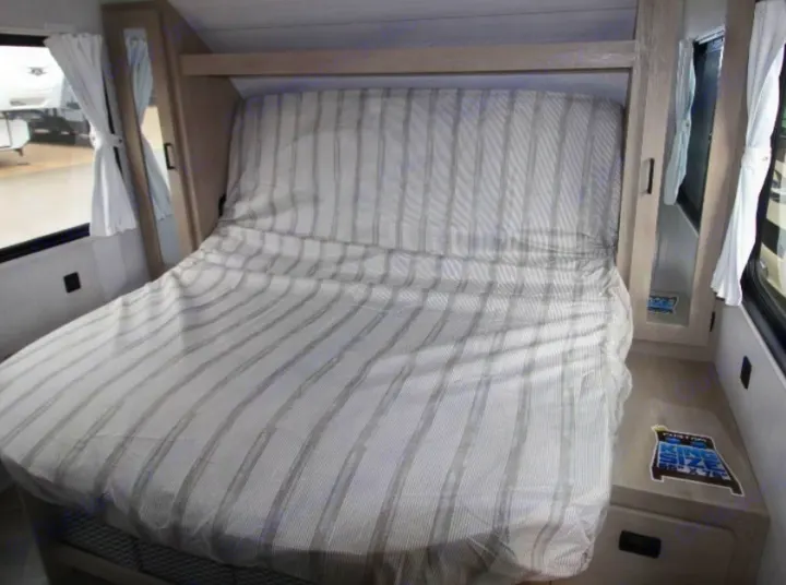 Cozy RV rental bedroom with striped bed, windows, and built-in storage, ideal for compact living.. Forest River Wildwood XLite View 2024