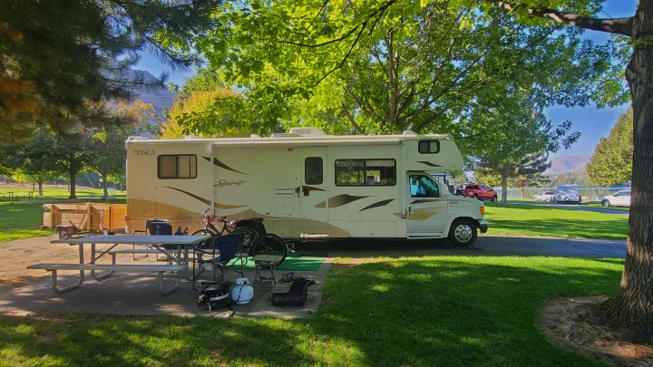 Relaxing RV rental getaway: An Itasca Spirit motorhome parked at a scenic campground. Features a picnic table, bikes, and grill near a lake.. Itasca Spirit 2007