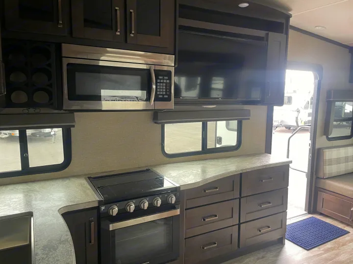 Bright RV rental interior features a modern kitchen: stainless microwave, oven, TV, and dark cabinetry with ample storage.. Grand Design Reflection 2021
