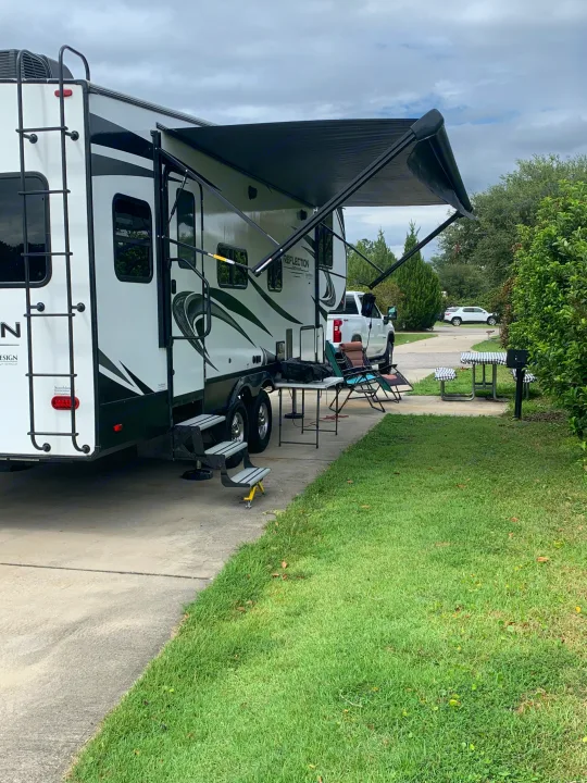 RV rental at a serene campsite: white travel trailer with extended awning, outdoor chairs, and a picnic table on a paved site.. Grand Design Reflection 2021