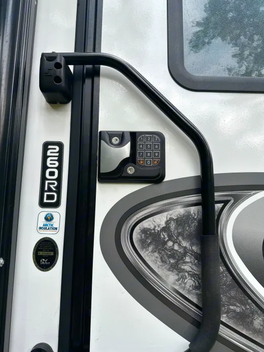Close-up of an RV rental door featuring a digital keypad entry system, robust grab handle, and Arctic Insulation branding.. Grand Design Reflection 2021