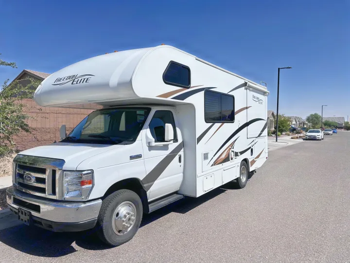 Bright white Ford Freedom Elite RV rental, detailed with brown and black graphics, parked on a residential street under a clear blue sky.. Thor Freedom Elite 2016