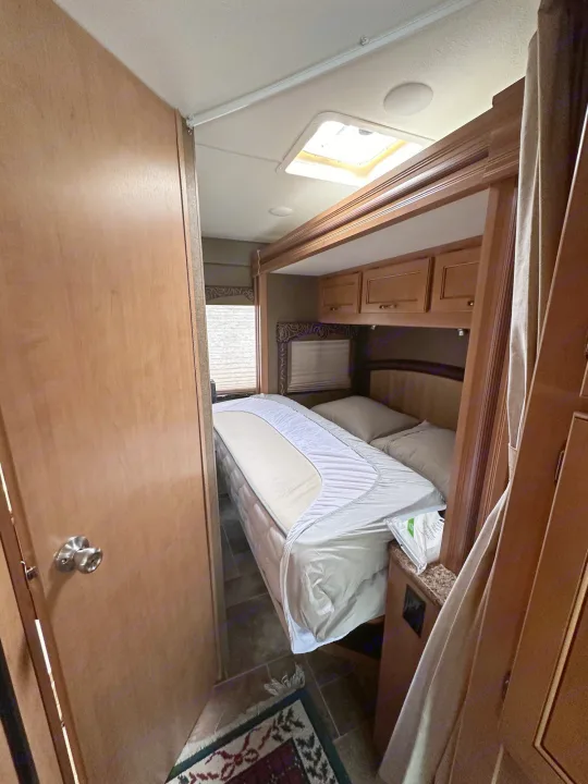 Bedroom view in an RV rental, featuring a mattress, overhead cabinets, and a window with blinds. Ready for travel.. Thor Freedom Elite 2016