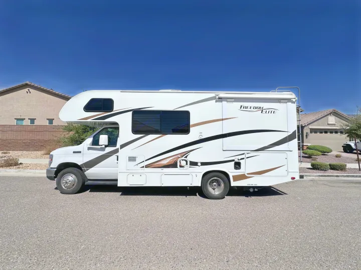 White Class C motorhome rv rental with brown graphics, parked on a sunny street, ready for travel.. Thor Freedom Elite 2016
