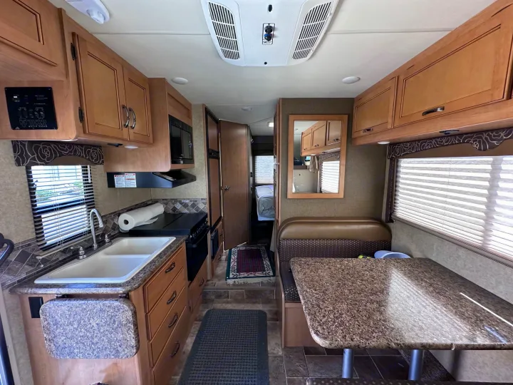 Experience comfort in this RV rental interior: a well-equipped kitchen, dining booth, and corridor leading to the sleeping area.. Thor Freedom Elite 2016