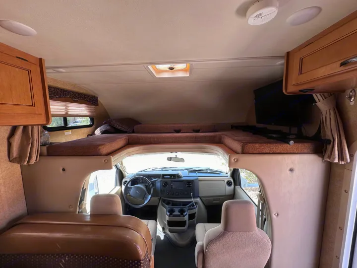 Inside an RV rental, this view shows the motorhome's cockpit & cozy cab-over bunk, ready for adventure.. Thor Freedom Elite 2016