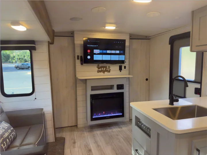 Step inside this RV rental: a modern living space featuring a TV, electric fireplace, and kitchen island.. Heartland RVs North Trail 2023