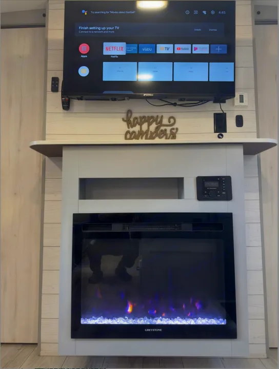 Cozy RV rental interior featuring a smart TV, a 'happy campers' sign, and a glowing electric fireplace below.. Heartland RVs North Trail 2023