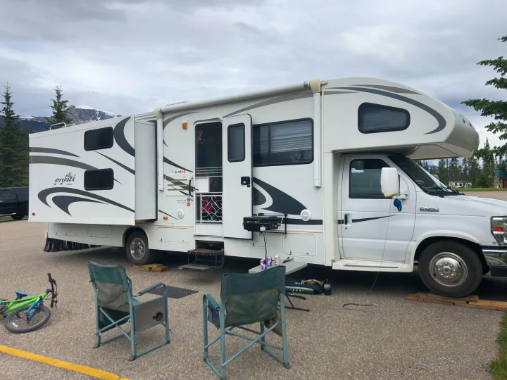 A white Greyhawk RV rental is set up with chairs, a grill, and a bike at a mountain campsite under a cloudy sky.. Jayco Greyhawk 2010