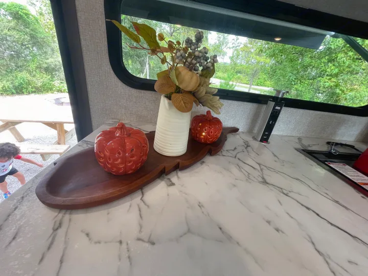 RV rental kitchen: white counter, fall decor, pop-up outlet. Child plays outside near picnic table.. Dutchmen Kodiak Ultra Lite 2021
