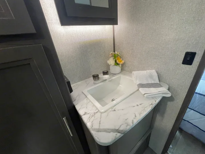 RV rental's compact bathroom features a white sink, marble counter, and floral decor, perfect for travel.. Dutchmen Kodiak Ultra Lite 2021
