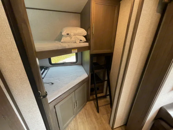 Cozy RV rental bunk beds with window view, storage, and access ladder. Ideal for family trips.. Dutchmen Kodiak Ultra Lite 2021