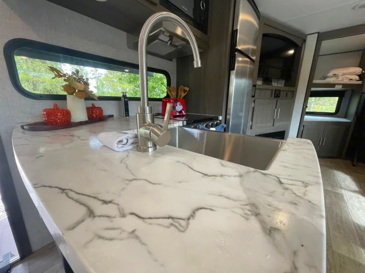 Spacious RV rental kitchen with modern marble-look counter, sink, appliances, and scenic window views.. Dutchmen Kodiak Ultra Lite 2021