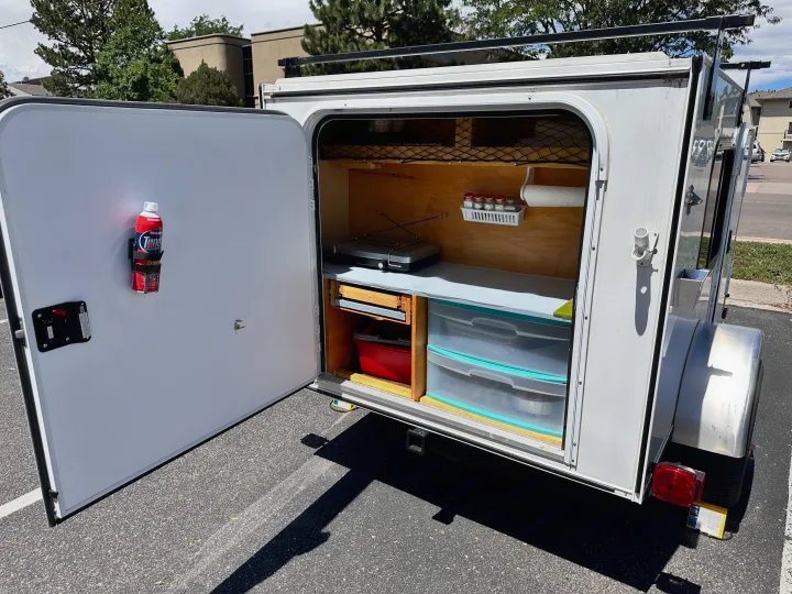 This RV rental teardrop camper showcases its organized outdoor kitchen with stove, spice rack, and storage.. Hiker Deluxe 2018